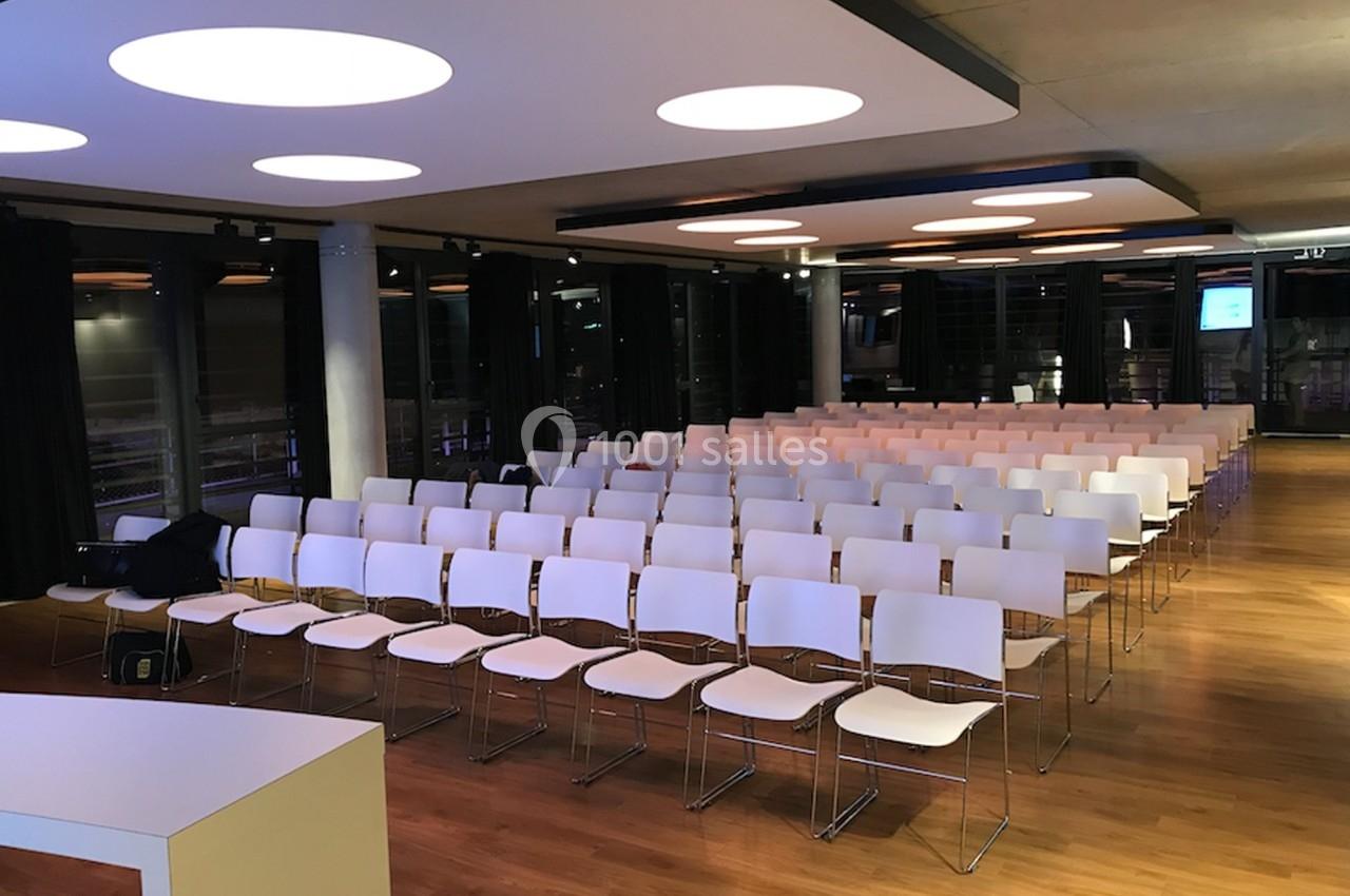 Salle de conférence moderne avec rangées de chaises blanches alignées et éclairage au plafond.