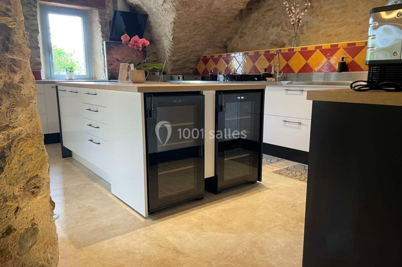 Cuisine moderne avec murs en pierre, îlot central équipé de caves à vin et crédence en carreaux colorés.