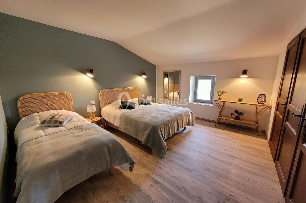 Chambre lumineuse avec deux lits simples, mur vert pastel, parquet clair et mobilier en bois naturel.