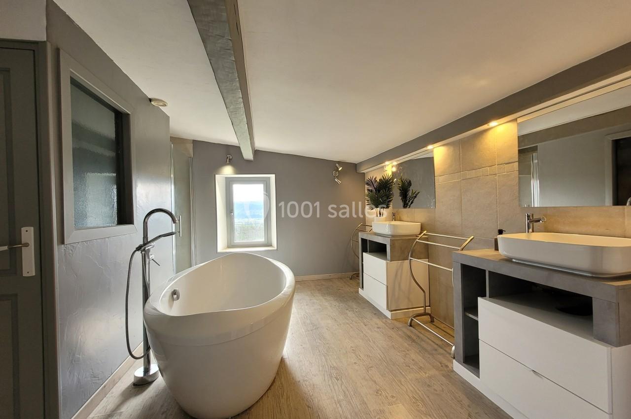 Salle de bain moderne avec baignoire îlot, meuble double vasque, éclairage intégré et sol en bois clair.