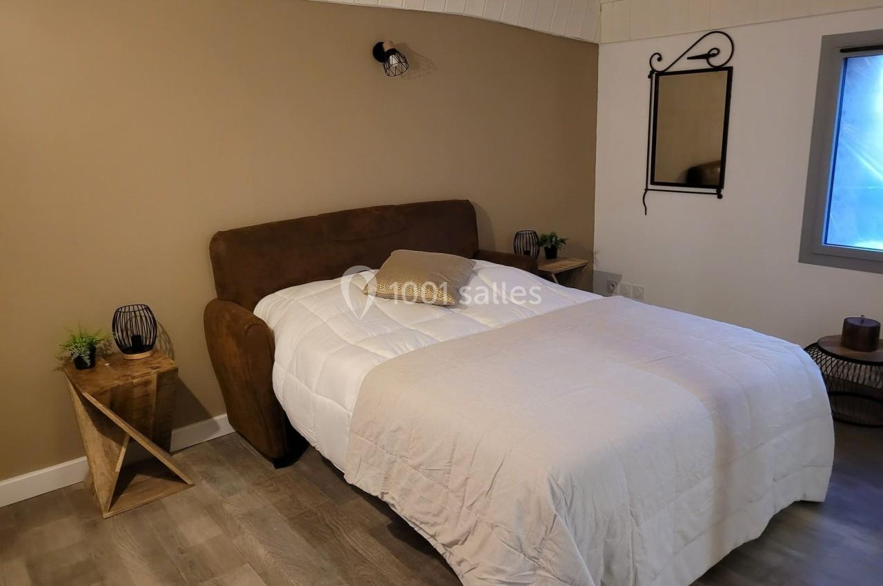 Lit double avec une couverture blanche, encadré par deux tables de chevet en bois, dans une chambre au décor sobre.