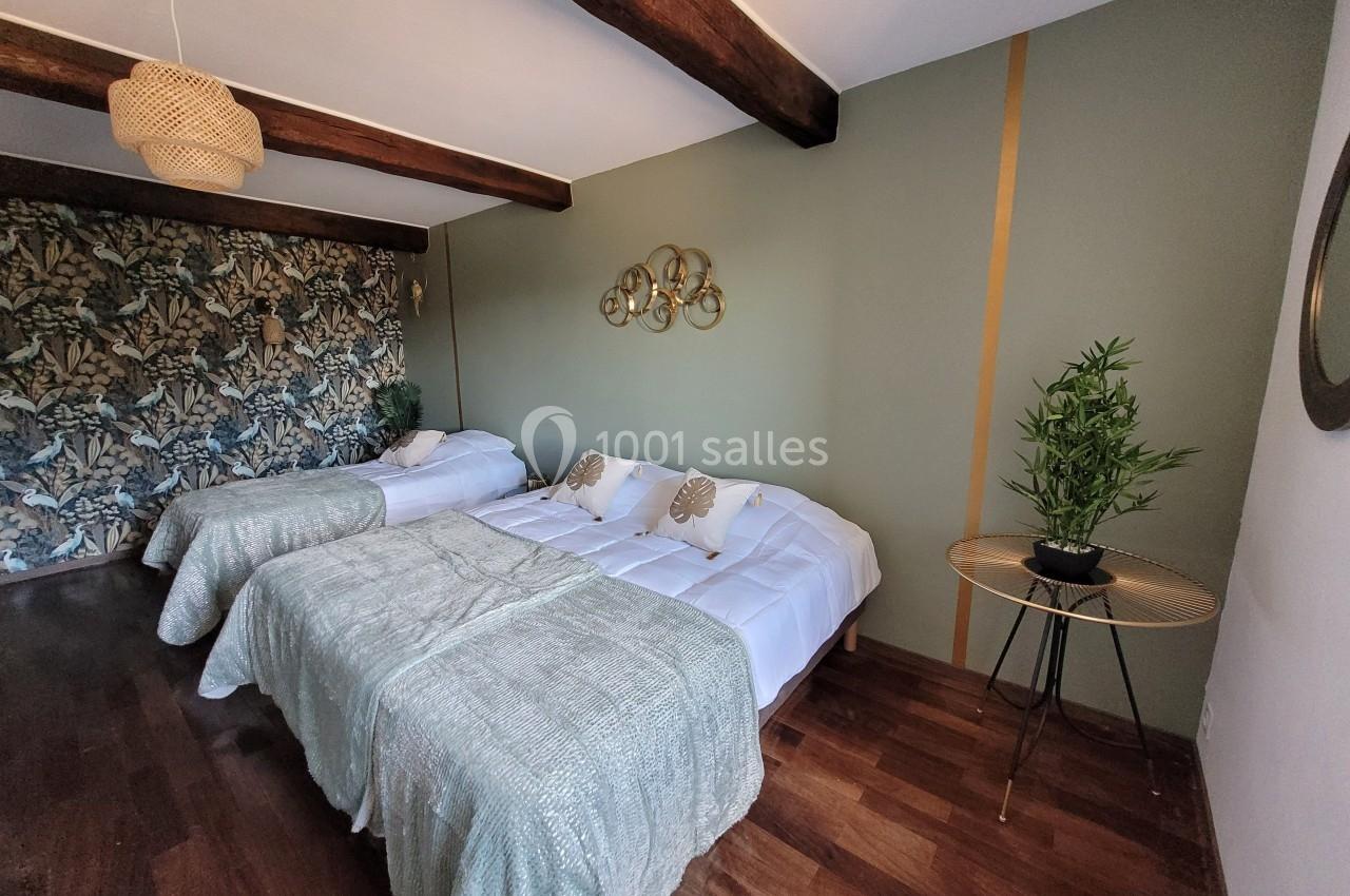 Chambre avec deux lits doubles, parquet, mur décoré de papier peint floral, plantes et décoration murale dorée.