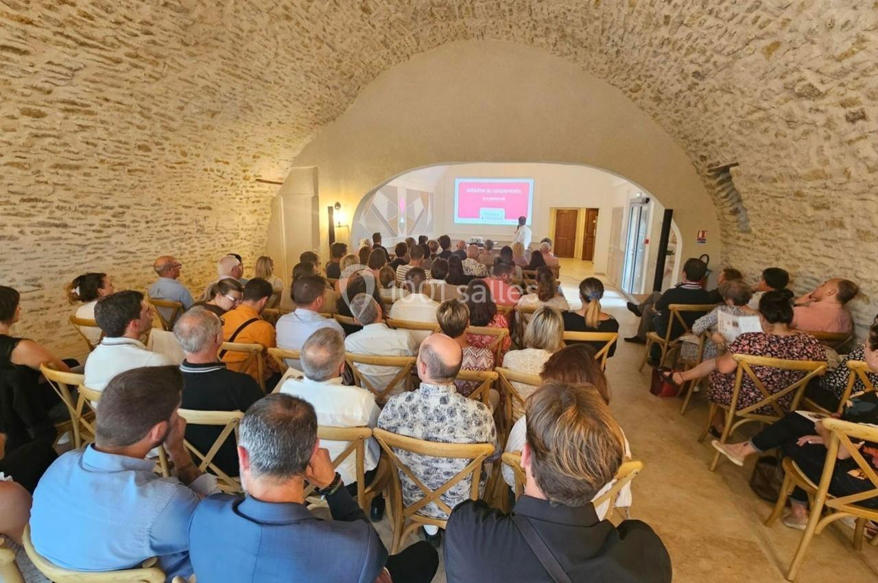 Salle voûtée en pierre avec des participants assis, assistant à une présentation projetée sur un écran.