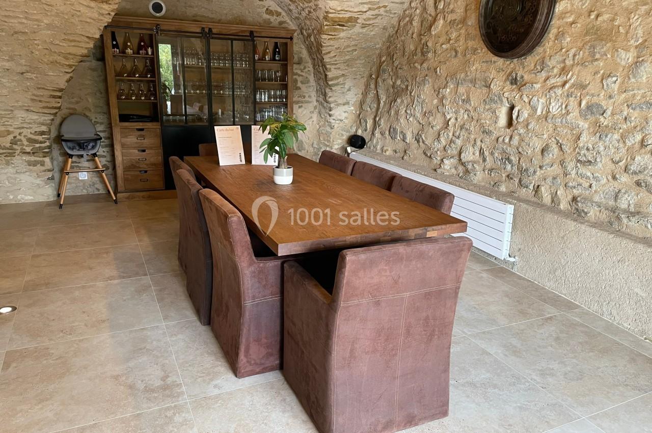 Table en bois avec six chaises rembourrées dans une pièce en pierre avec une armoire vitrée en arrière-plan.