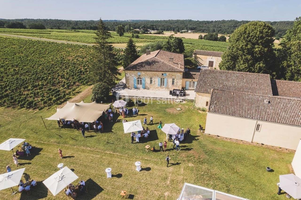 Vue aérienne d'un domaine avec des vignes, des bâtiments en pierre et un événement en plein air sous des tentes.