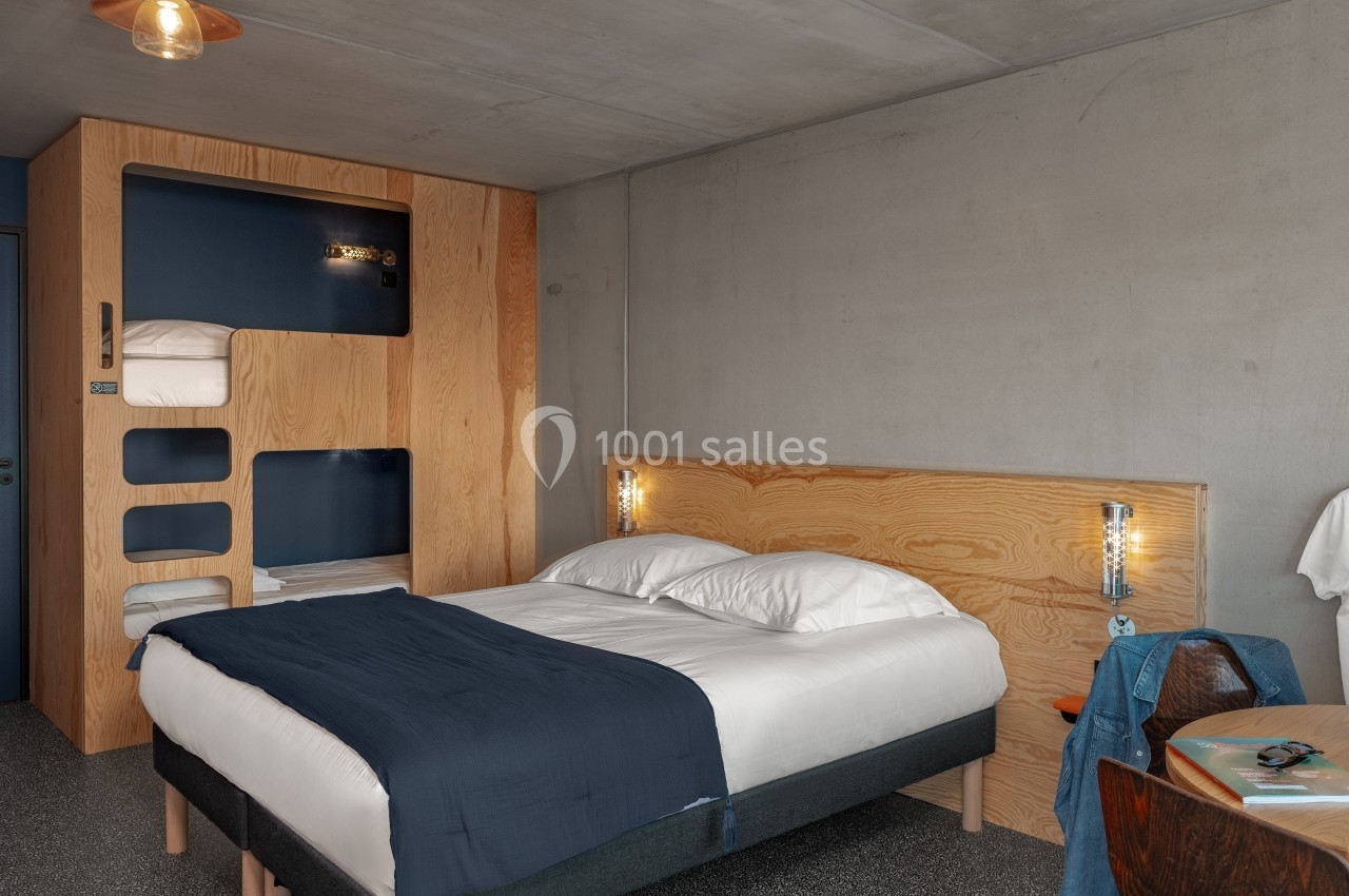 Chambre moderne avec lit double, literie bleue, lits superposés intégrés en bois et éclairage minimaliste.