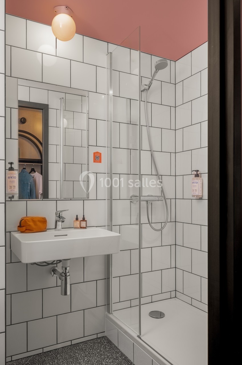 Salle de bain moderne avec douche à l'italienne, carrelage blanc, lavabo suspendu et éclairage mural.