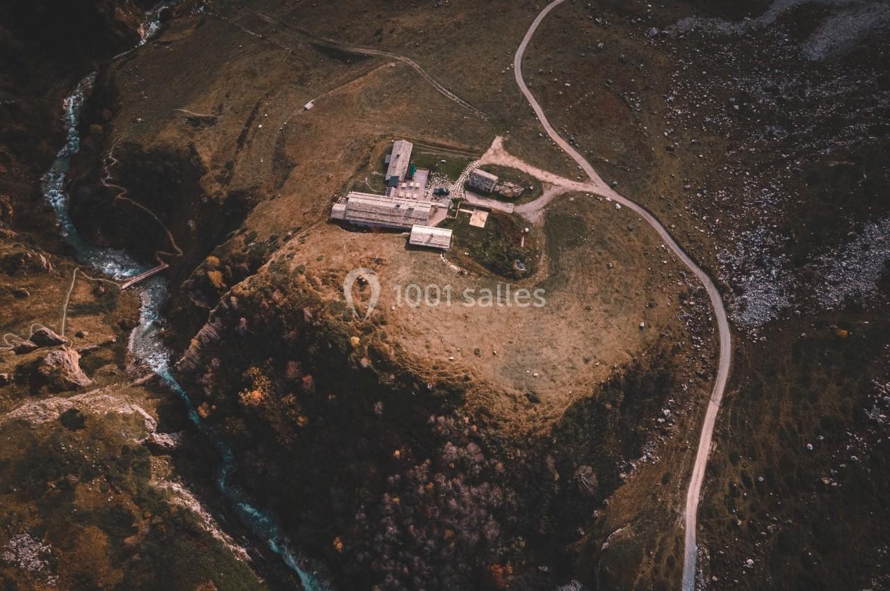 Vue aérienne d'un bâtiment isolé sur une colline entourée de sentiers, d'un ruisseau et de paysages naturels.