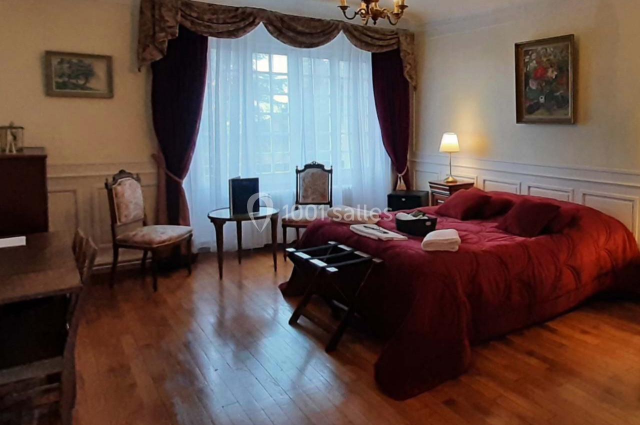 Chambre lumineuse avec lit double, rideaux rouges, parquet, mobilier classique et lumière d'une lampe de chevet.