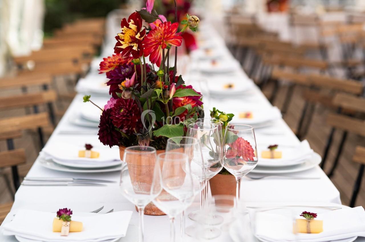 Table dressée dans une tente, ornée de bouquets de fleurs rouges et jaunes, avec vaisselle et couverts alignés.