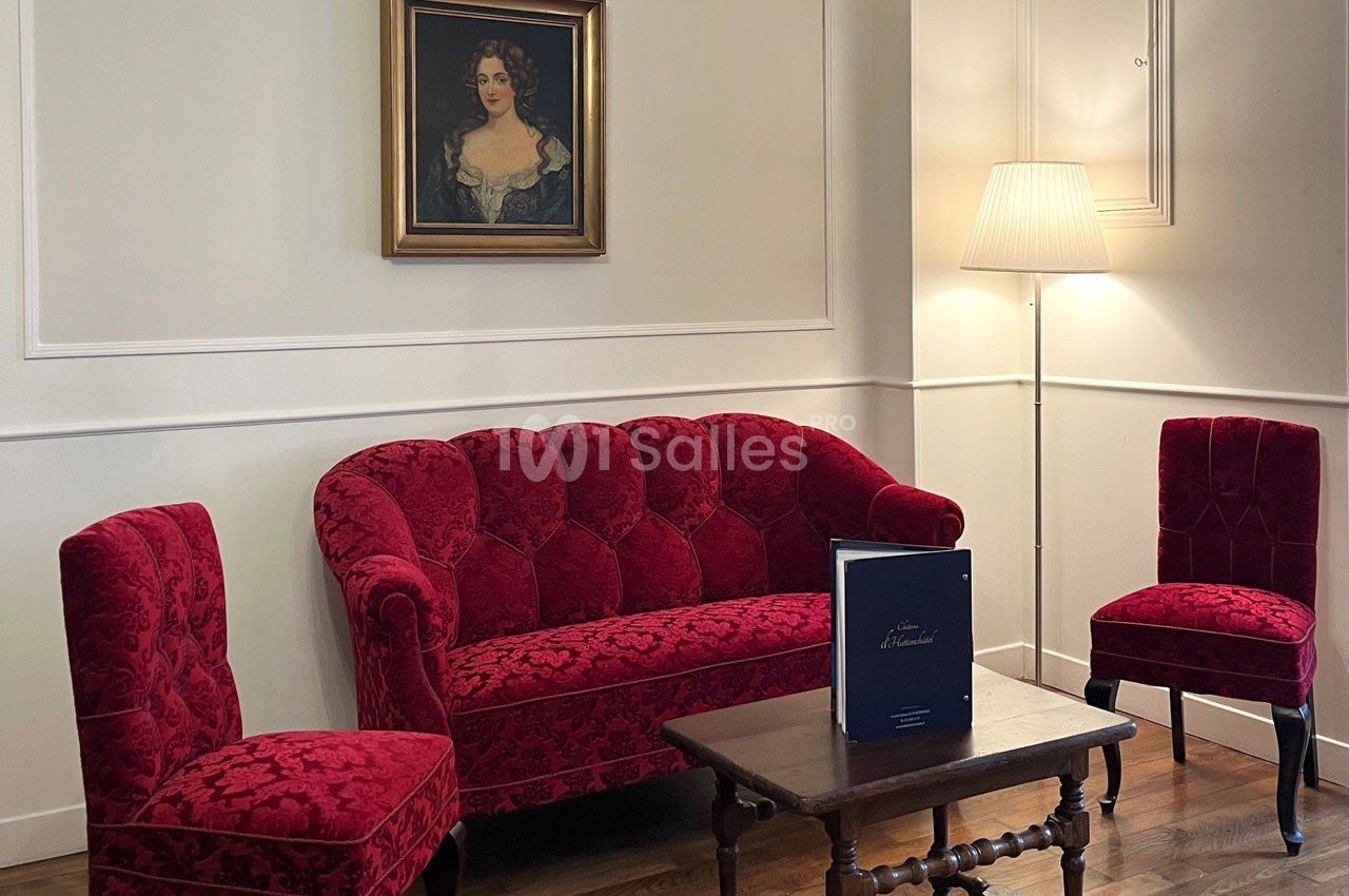 Salon avec canapé et chaises en velours rouge, table basse en bois, lampe sur pied et tableau au mur.