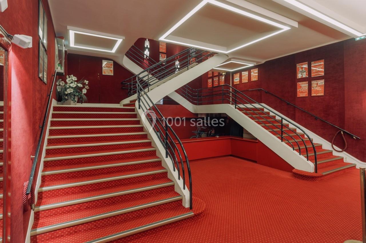 Escalier intérieur à double volée avec tapis rouge, murs rouges décorés d'affiches et éclairage géométrique au plafond.
