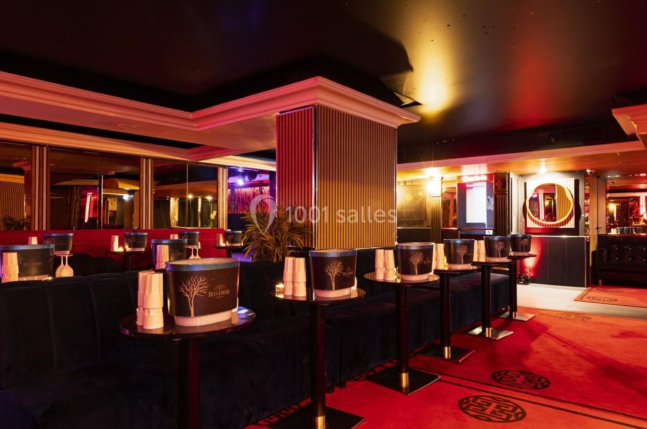 Salle de club avec banquettes rouges, tables basses noires et éclairage tamisé dans une ambiance nocturne.