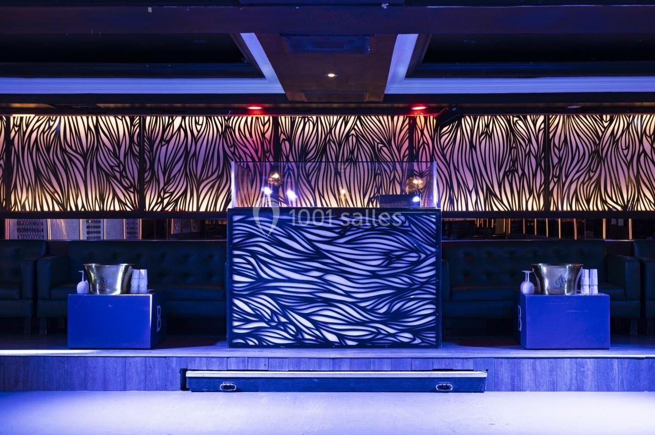Pupitre central décoré de motifs ondulés, entouré de banquettes et seaux à champagne dans un espace lumineux.
