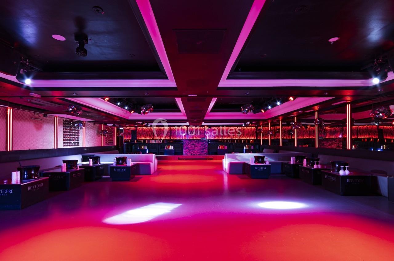 Salle de réception moderne avec éclairage rouge et violet, banquettes alignées et piste centrale dégagée.