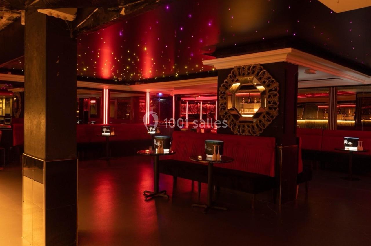 Salle de bar avec banquettes rouges, tables basses éclairées et plafond étoilé dans une ambiance tamisée.