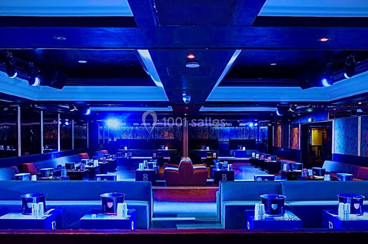 Salle de réception moderne avec éclairage bleu, tables dressées et banquettes alignées dans un cadre élégant.