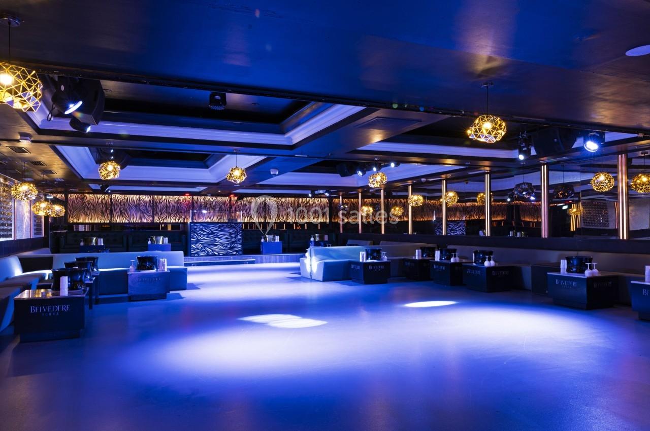 Salle de réception moderne avec éclairage bleu, banquettes alignées et tables basses noires.