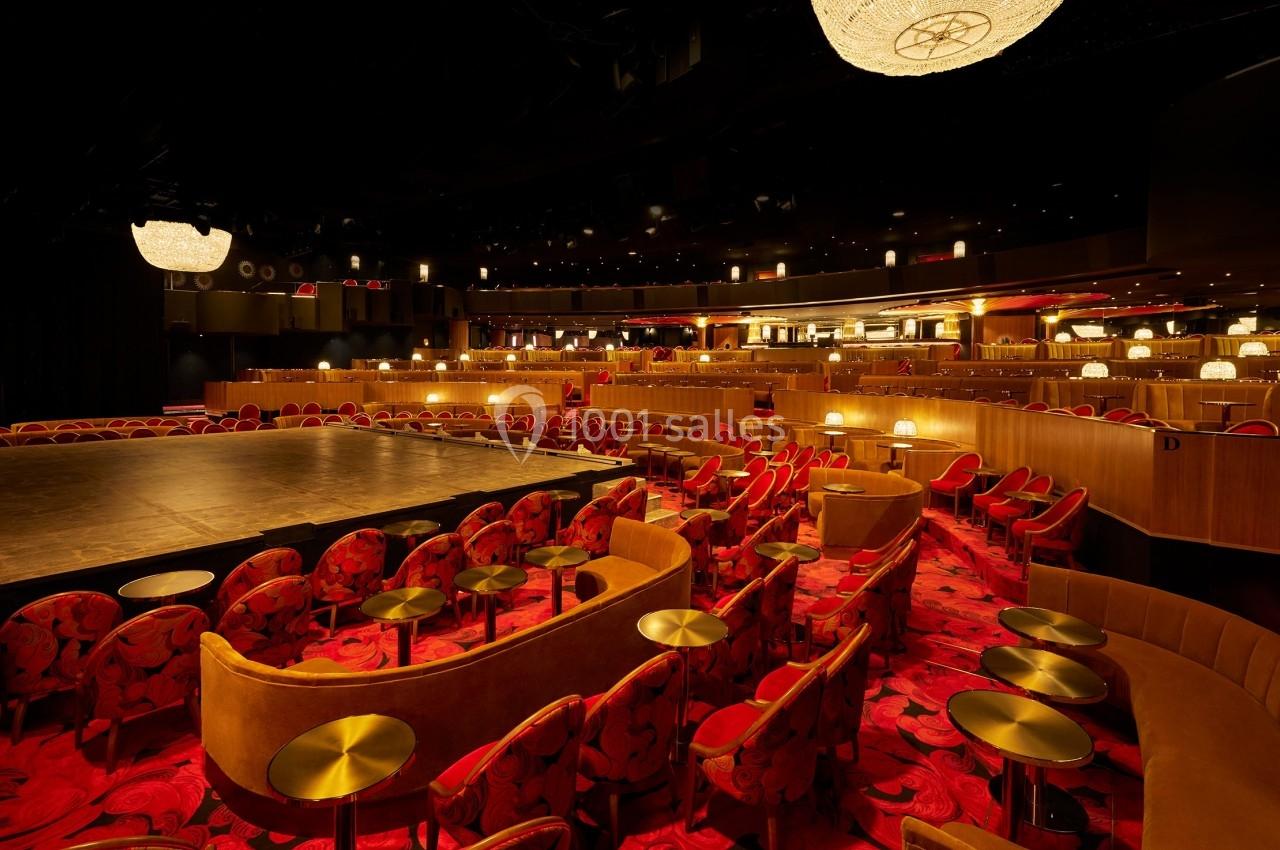 Salle de spectacle avec scène centrale, sièges rouges et dorés, éclairage tamisé et ambiance élégante.