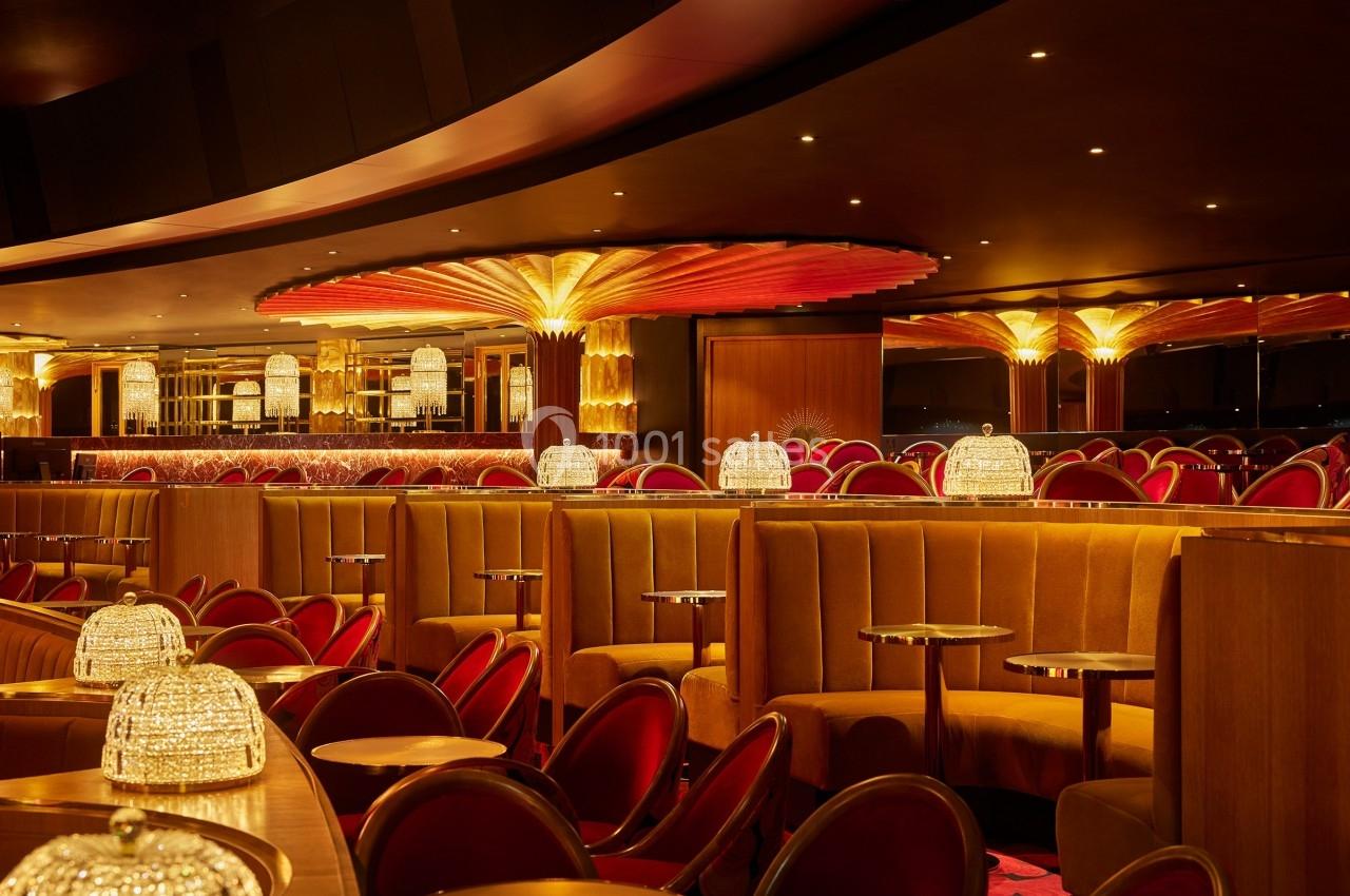 Salle de restaurant élégante avec banquettes en velours, chaises rouges et éclairage chaleureux sous un plafond décoratif.