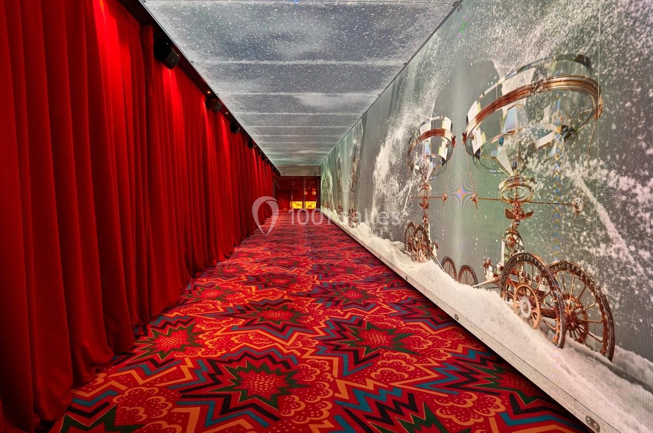 Couloir décoré de rideaux rouges, tapis coloré et mur orné d'engrenages métalliques sur fond neigeux.