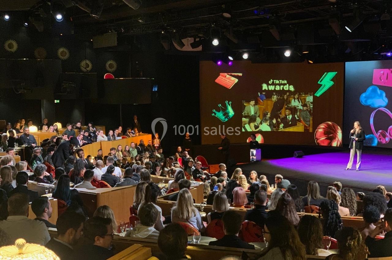 Salle comble lors d'une cérémonie de remise de prix, avec une scène éclairée et un public attentif.