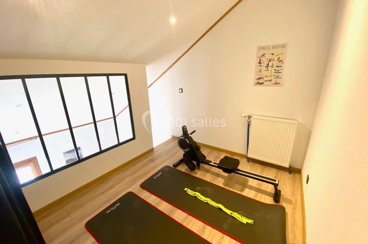 Salle de sport à domicile avec deux tapis de sol, un rameur et un poster d'exercices sur un mur blanc.