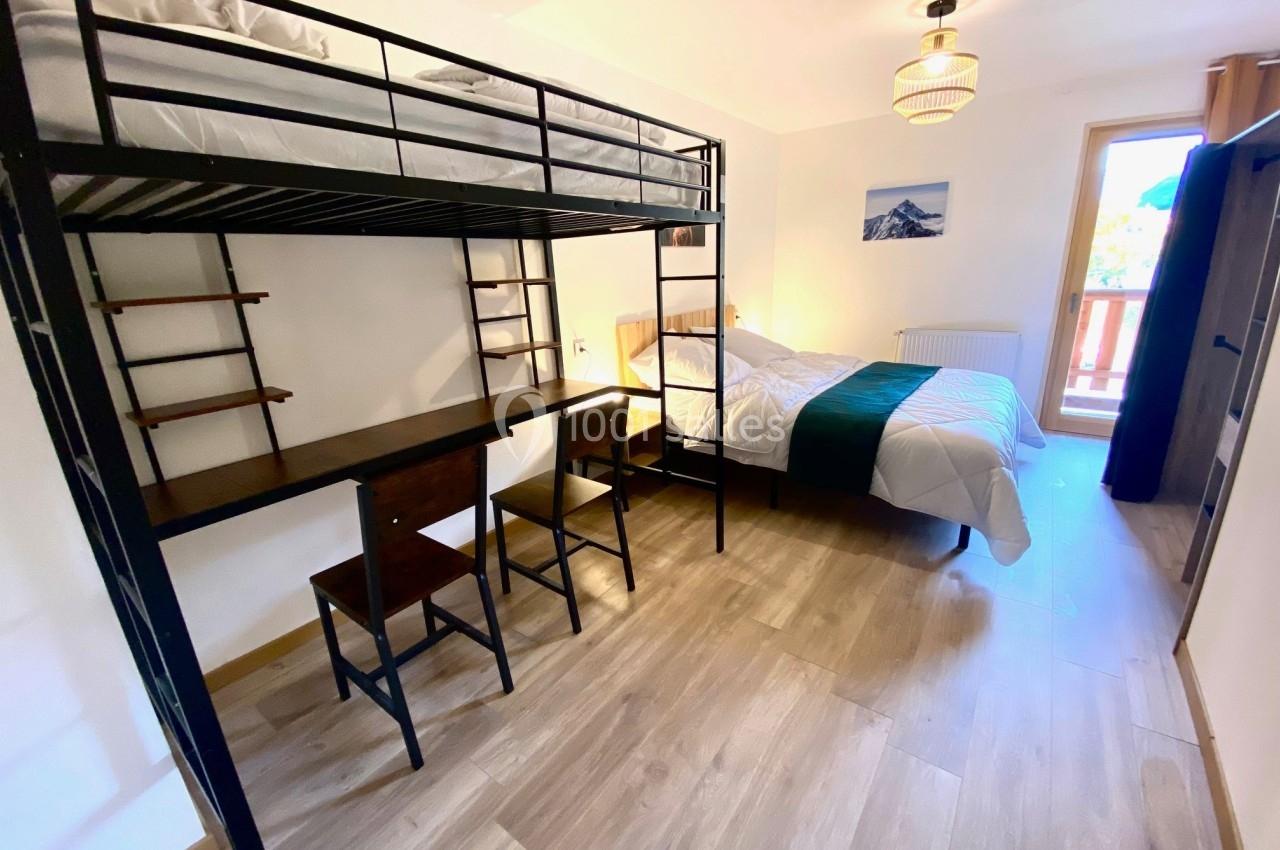 Chambre lumineuse avec lit superposé, bureau intégré, lit double, parquet clair et accès à un balcon.