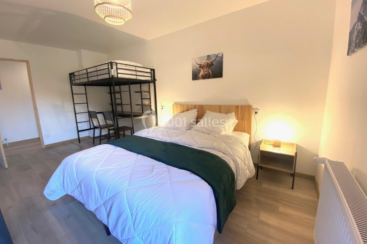Chambre lumineuse avec un lit double, un lit superposé, un bureau, et une décoration murale dans un style épuré.