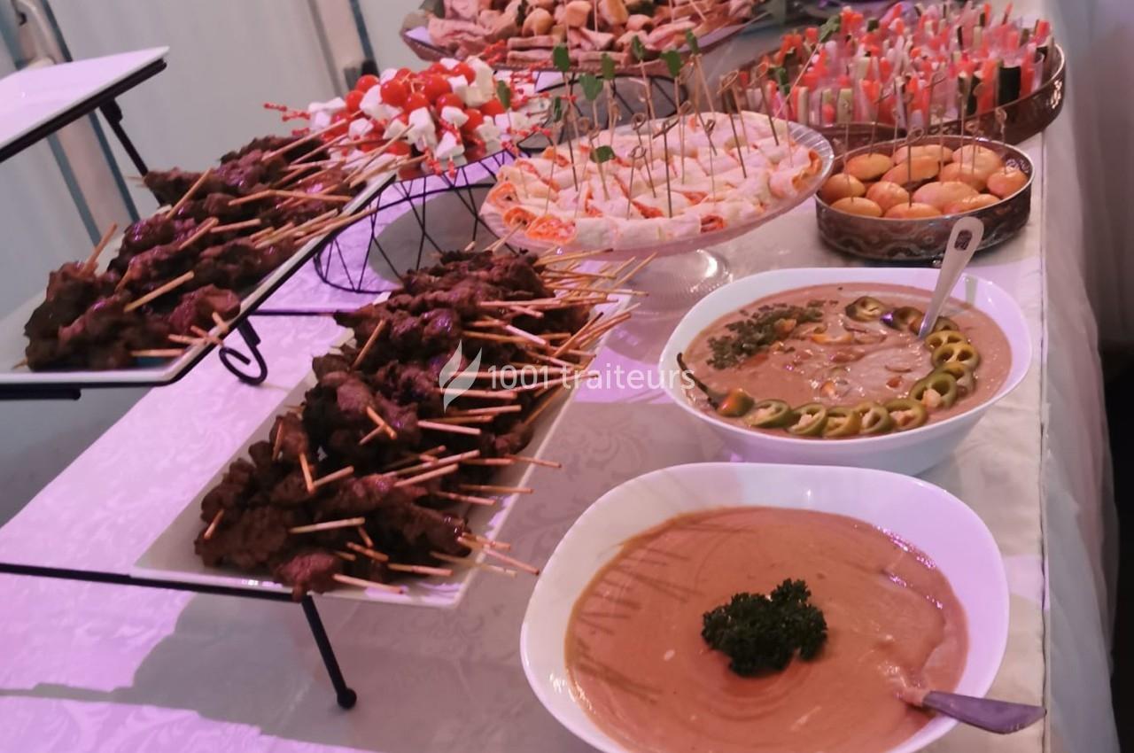 Buffet avec brochettes de viande, verrines, pains garnis et sauces présentés sur une table blanche.
