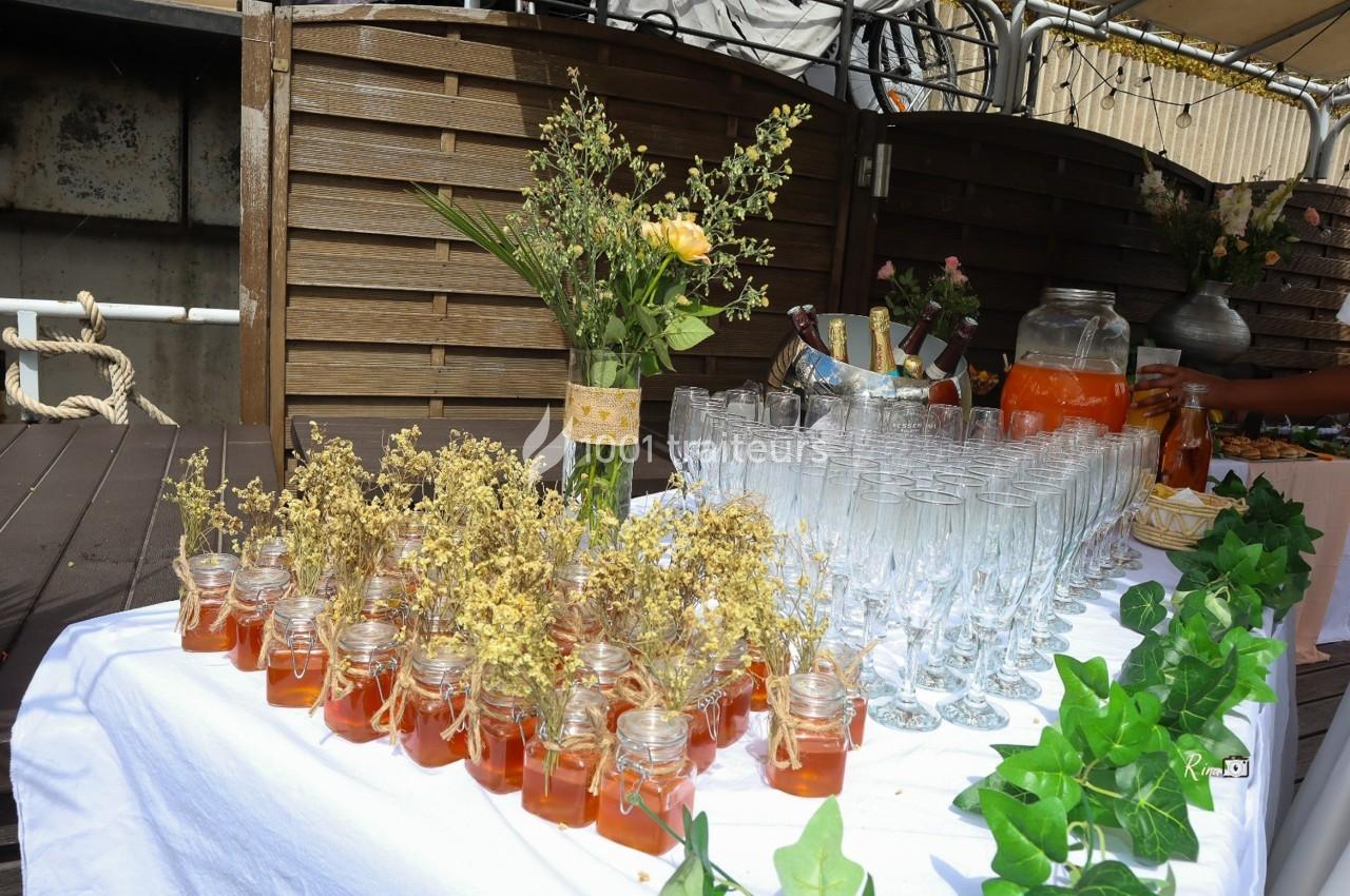 Table décorée avec des pots de miel, des fleurs séchées, des verres à champagne et une carafe de boisson orange.