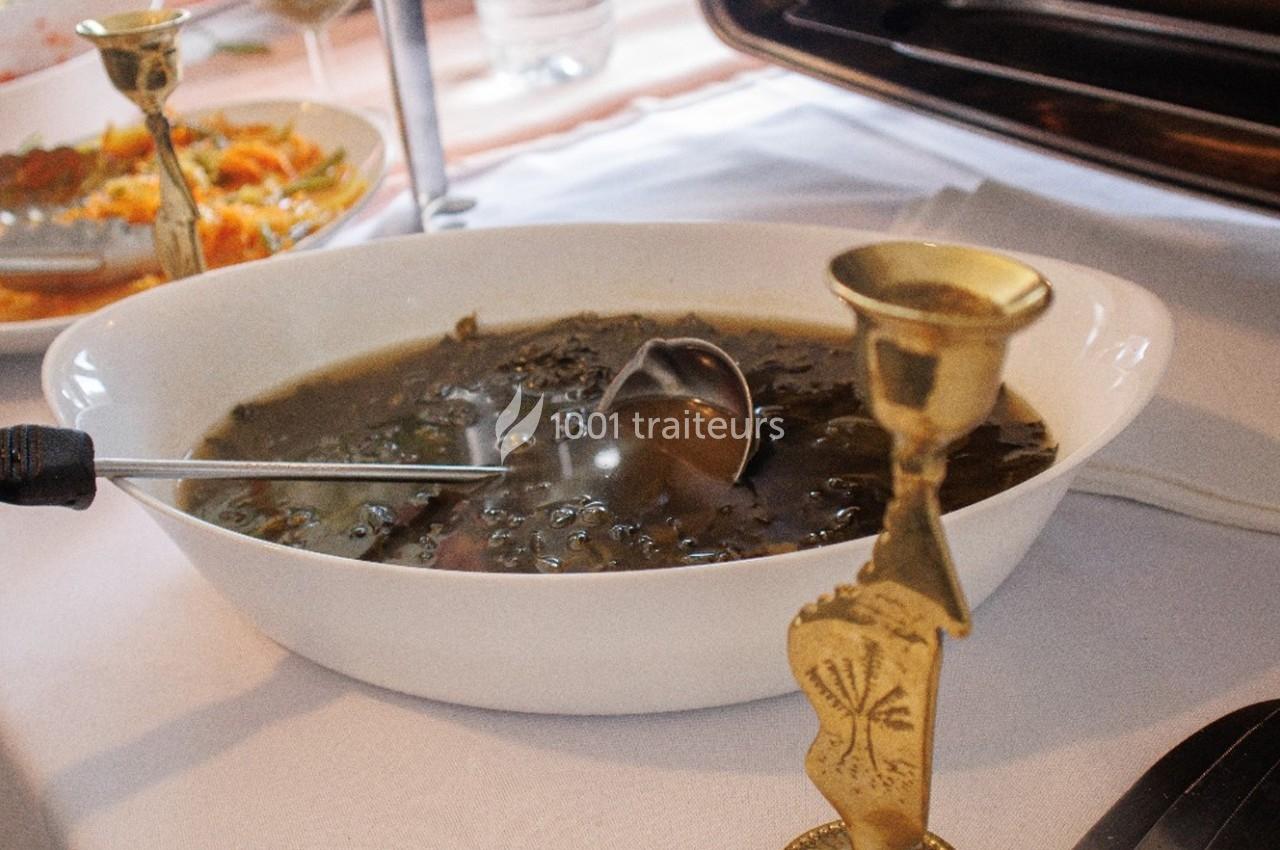 Plat de soupe aux légumes verts servi dans un saladier blanc avec une louche en métal sur une table dressée.