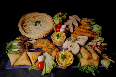 Plateau de charcuterie et fromages avec fruits, légumes et une bouteille de vin rouge, présenté sur une table en extérieur.