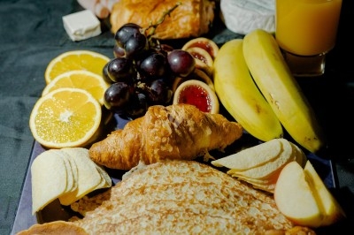 Plateau de charcuterie et fromages avec fruits, légumes et une bouteille de vin rouge, présenté sur une table en extérieur.