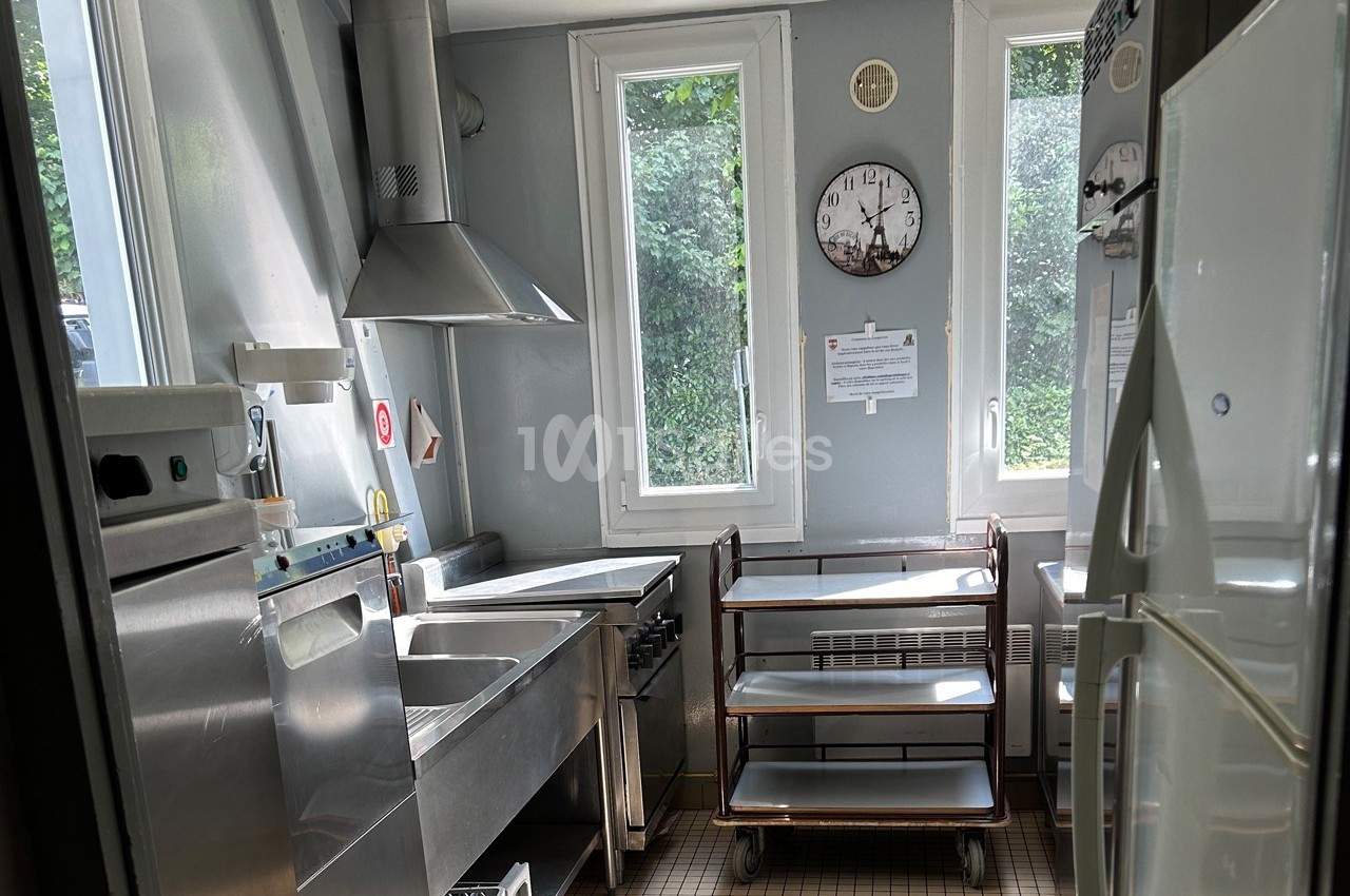 Cuisine professionnelle lumineuse avec équipements en inox, fenêtres donnant sur un extérieur verdoyant.