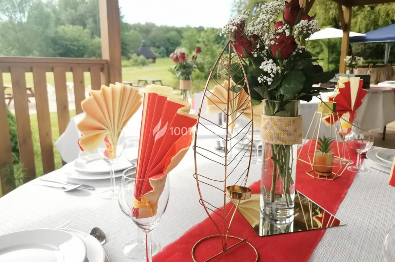Table décorée pour un événement avec nappes blanches, chemin de table rouge, fleurs et pliages de serviettes colorés.