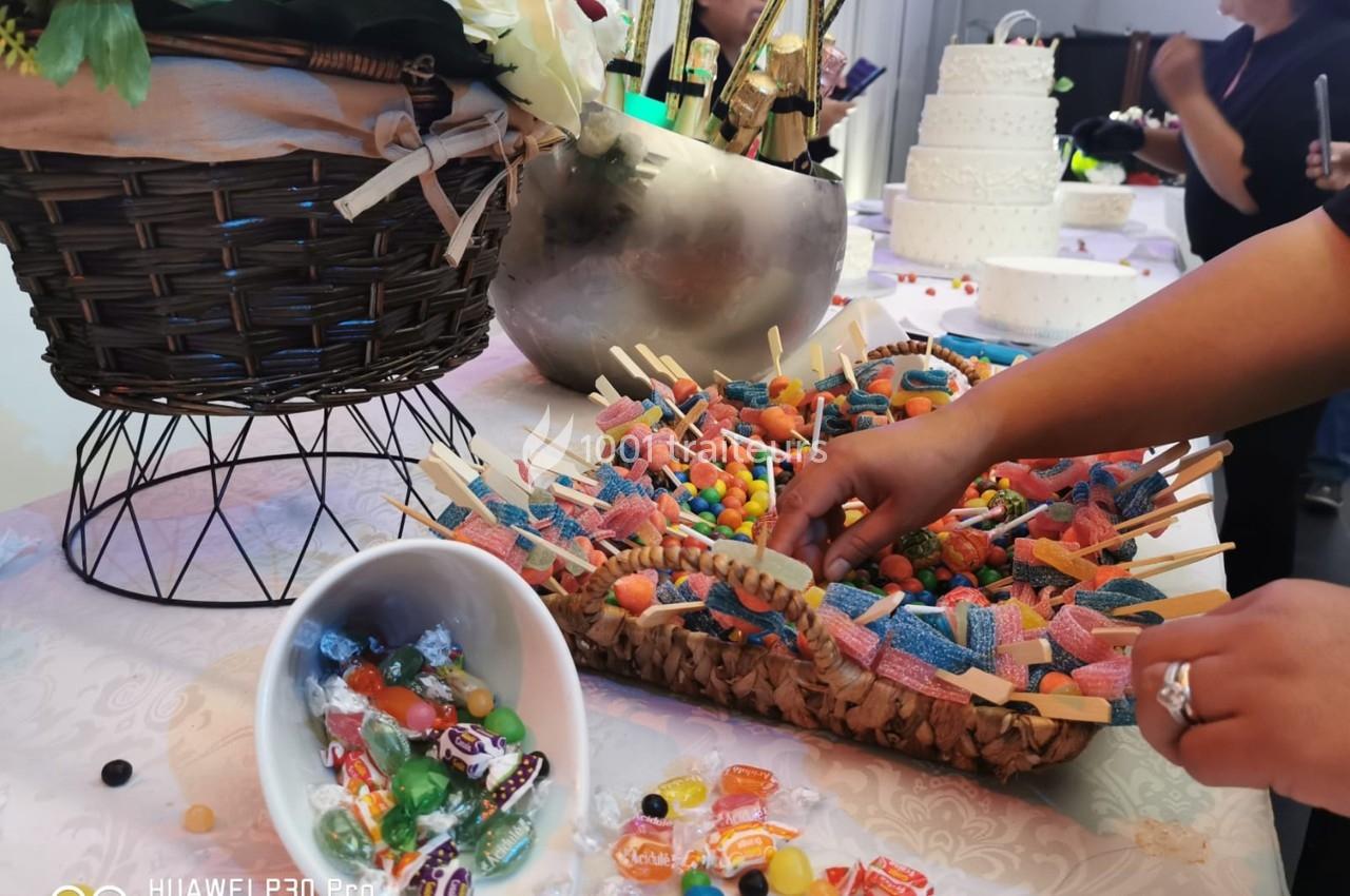 Un buffet de bonbons colorés avec des brochettes de friandises, un panier fleuri et un gâteau en arrière-plan.