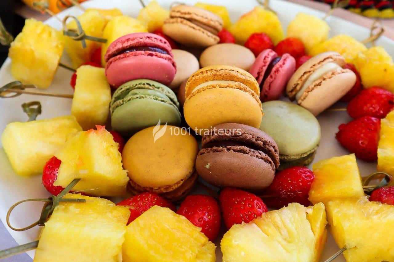 Assortiment de macarons colorés entourés de morceaux d'ananas et de fraises sur un plateau.