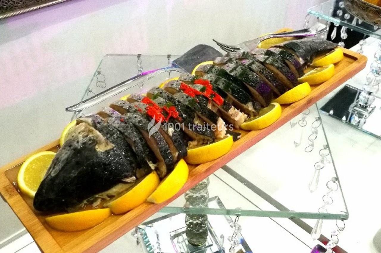 Poisson entier tranché, présenté sur un plateau en bois avec des quartiers de citron et une garniture rouge.