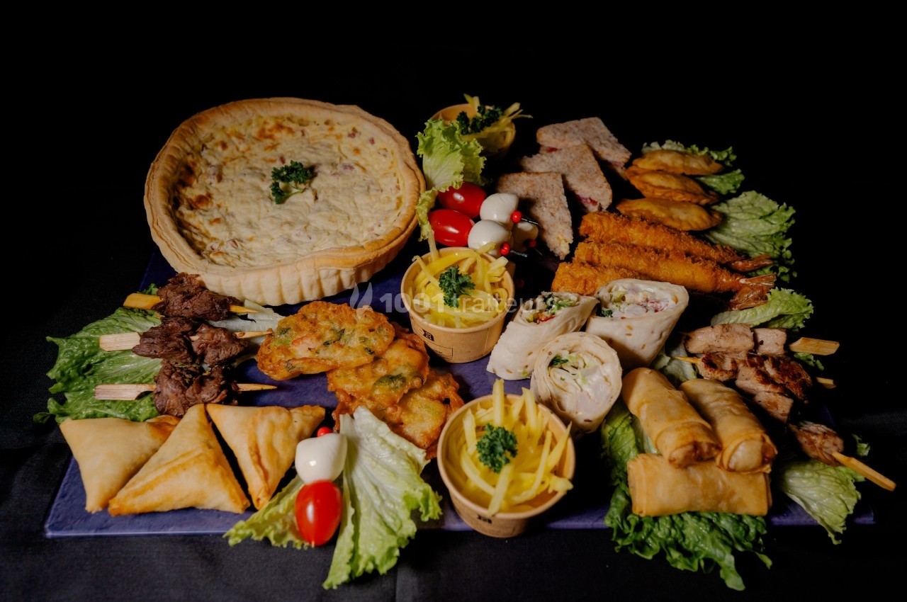 Plateau varié de mets salés comprenant quiche, brochettes, samoussas, rouleaux de printemps et autres amuse-bouches.