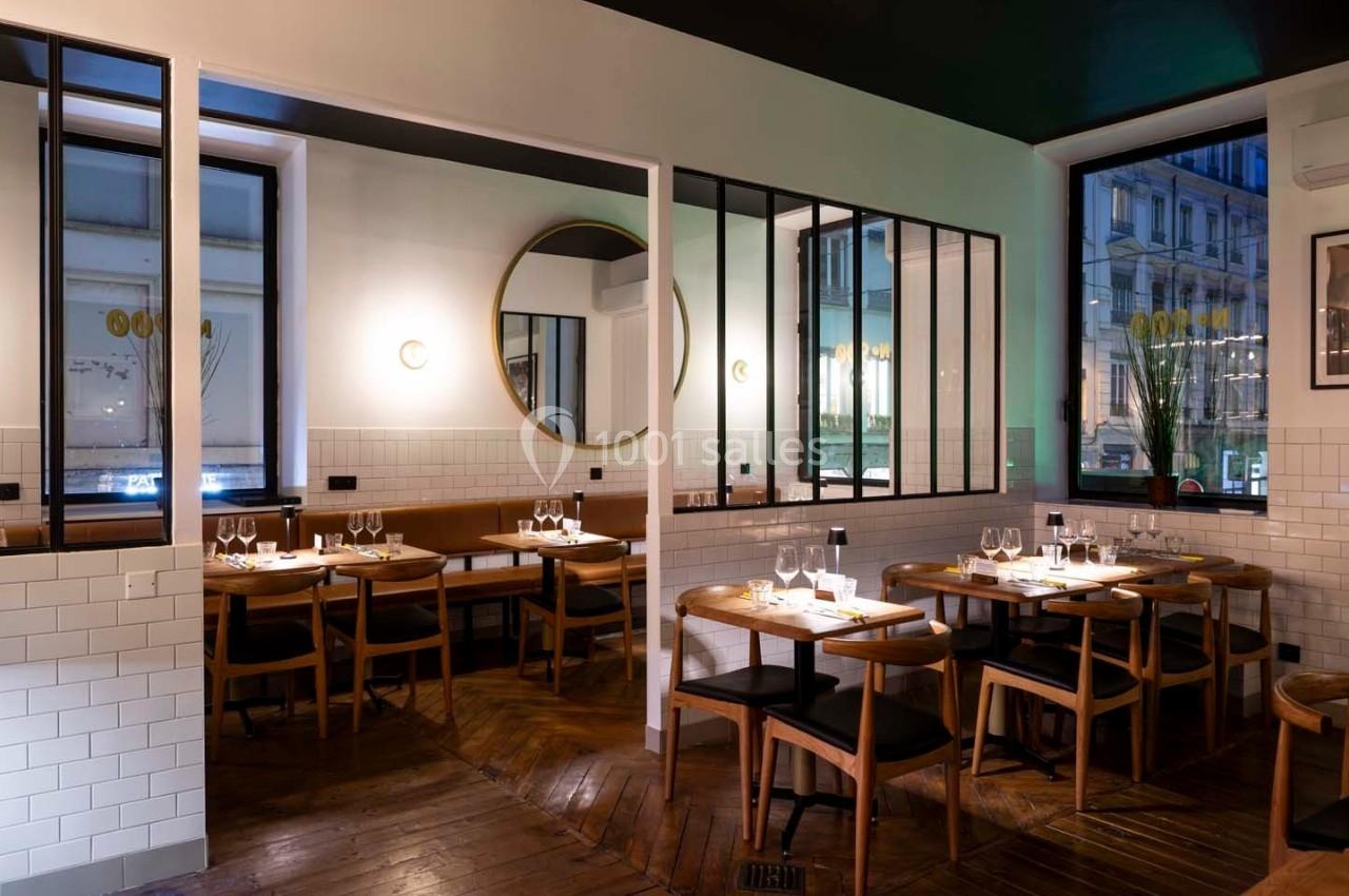Salle de restaurant moderne avec tables en bois, chaises noires, miroirs ronds et grandes fenêtres donnant sur l'extérieur.