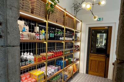 Étagères en bois remplies de produits alimentaires et ménagers dans une petite épicerie lumineuse avec sol carrelé.