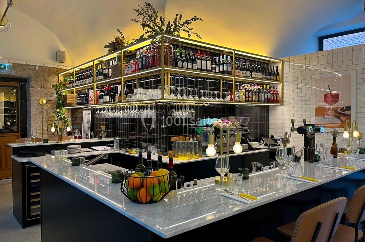 Comptoir de bar moderne avec étagères remplies de bouteilles, verres suspendus et décoration lumineuse.