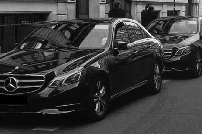 Miniature Regency Limo Coach #2 Alignement de véhicules noirs stationnés devant un bâtiment en pierre avec arcades, sous un ciel dégagé.