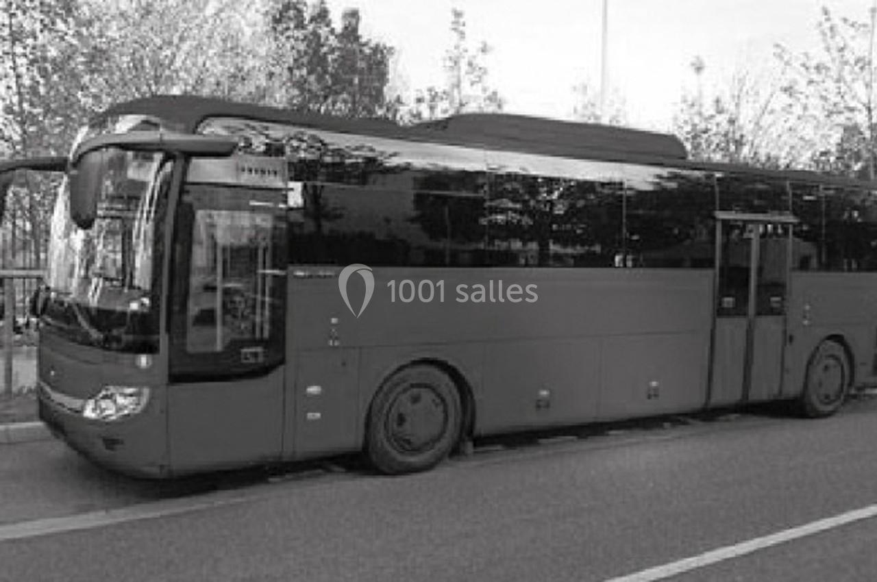 Autocar stationné sur le bord d'une route, avec des arbres en arrière-plan.