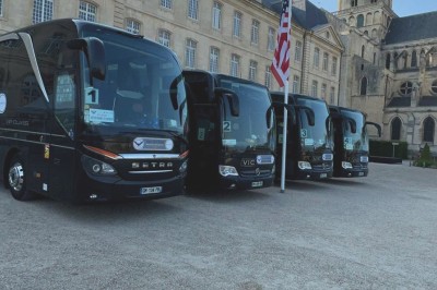 Miniature Regency Limo Coach #12 Alignement de véhicules noirs stationnés devant un bâtiment en pierre avec arcades, sous un ciel dégagé.