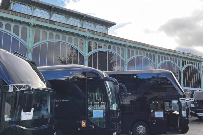 Miniature Regency Limo Coach #13 Alignement de véhicules noirs stationnés devant un bâtiment en pierre avec arcades, sous un ciel dégagé.