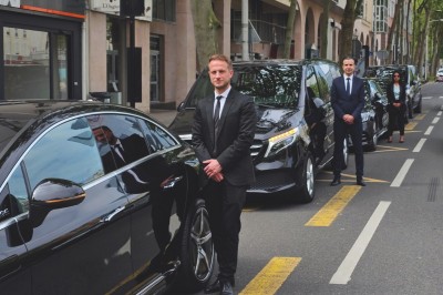 Miniature Regency Limo Coach #14 Alignement de véhicules noirs stationnés devant un bâtiment en pierre avec arcades, sous un ciel dégagé.