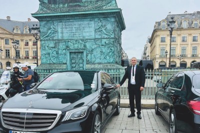 Miniature Regency Limo Coach #15 Alignement de véhicules noirs stationnés devant un bâtiment en pierre avec arcades, sous un ciel dégagé.
