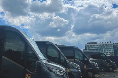 Miniature Regency Limo Coach #16 Alignement de véhicules noirs stationnés devant un bâtiment en pierre avec arcades, sous un ciel dégagé.